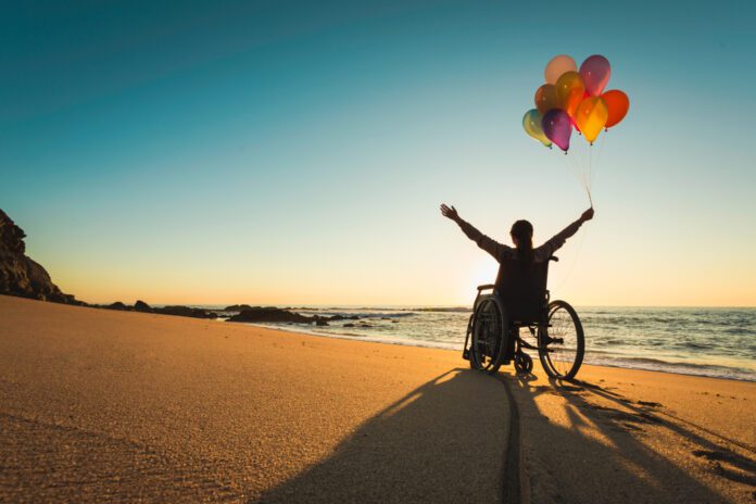 wheelchair user on beach with balloons. disability pride