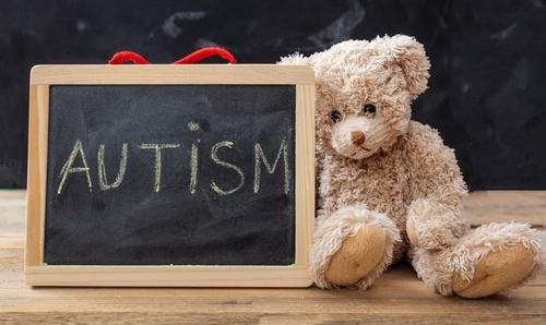 small blackboard with 'autism' written in chalk; sign is next to a teddy bear