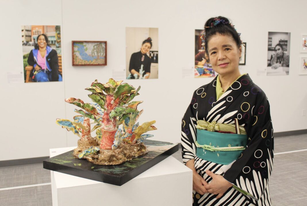 Envision Art BVI Artist Tomiyo Tajiri poses with her 3D ceramic sculpture depicting a Japanese landscape.