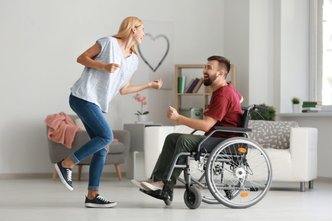 Man,In,Wheelchair,With,Beautiful,Woman,Dancing,At,Home interabled couple dancing and laughing