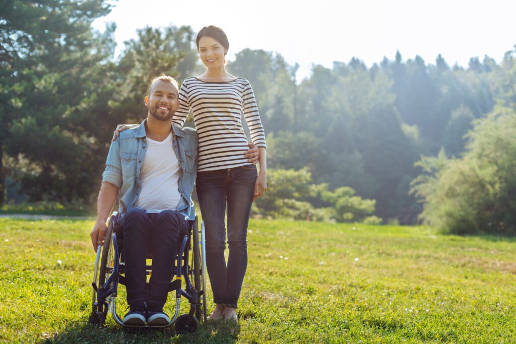 man in wheelchair side hugging a woman that is standing in a grassy field