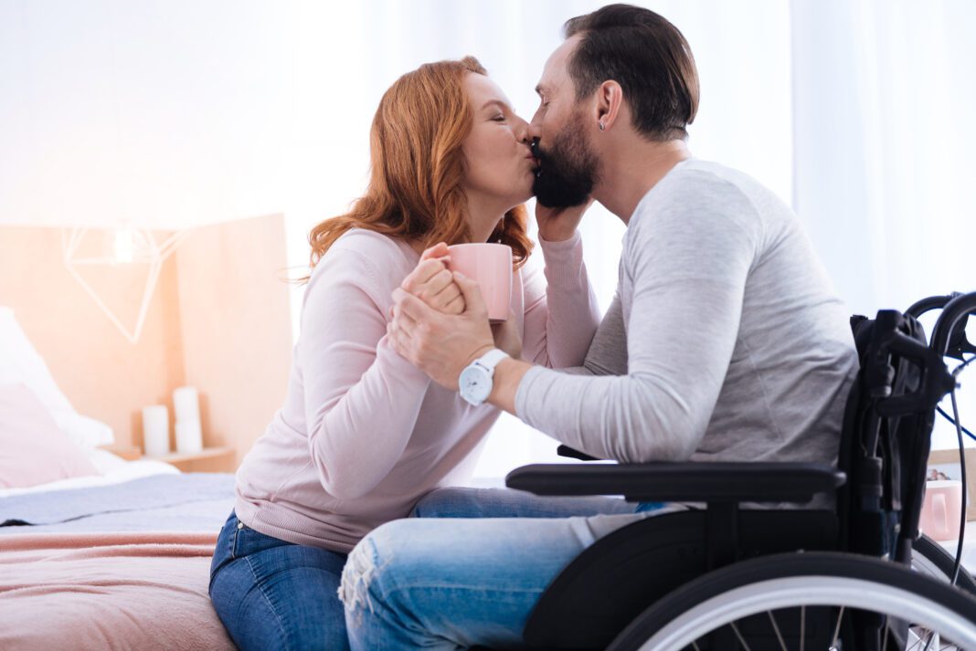 We,Love,Kissing.,Blond,Woman,Of,Middle,Age,And,A able-bodied woman holding cup while kissing man in a wheelchair