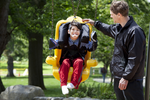 man pushing child on adaptive swing