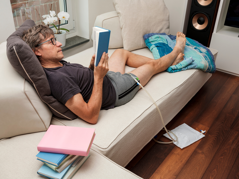 man laying down, reading book, using catheter