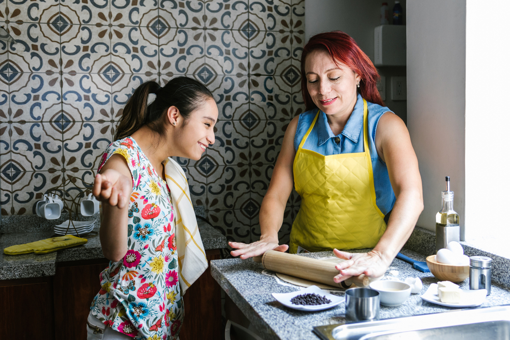 A Hispanic mother and daughter with disabilities cook together; roll out taco tortilla