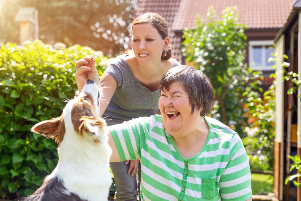 caregiver with elder women with disabilities and a companion animal, feeding eco-friendly dog treat