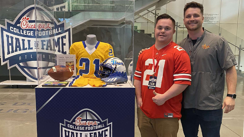 Caden Cox (left) stands next to his Hocking College football jersey on display at the College Football Hall of Fame. He's joined by his brother, Zane (right), who inspired him to pursue football.
