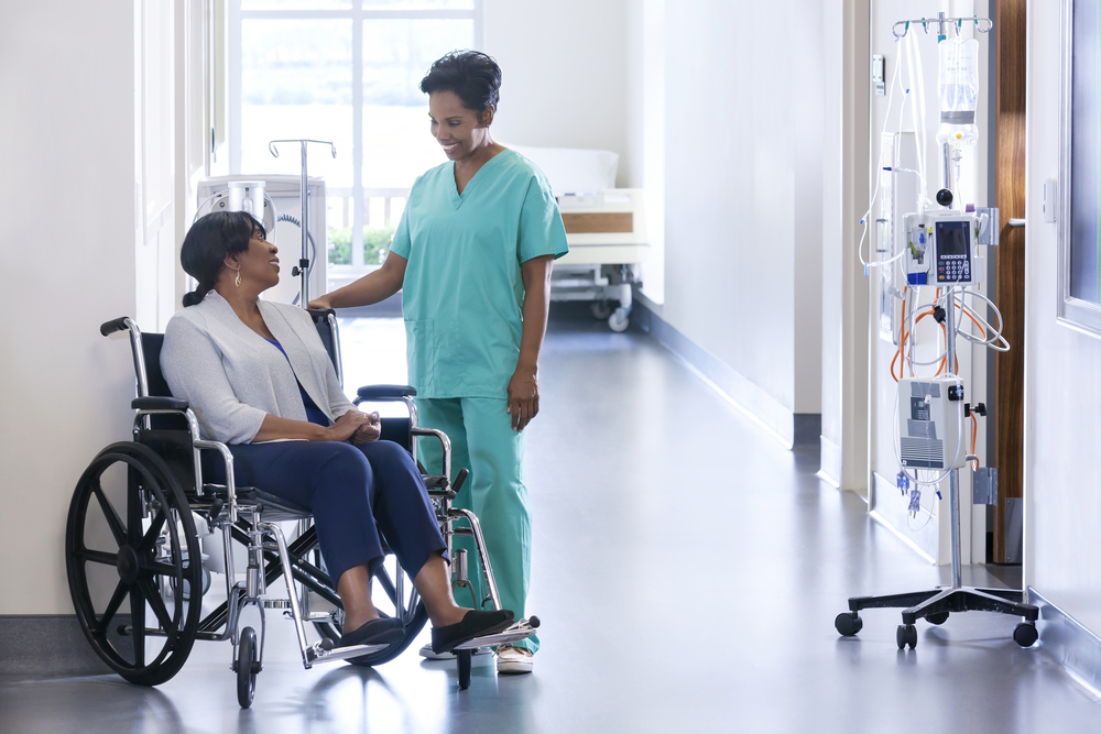older female patient, seated in wheelchair, smiling at female nurse in hallway