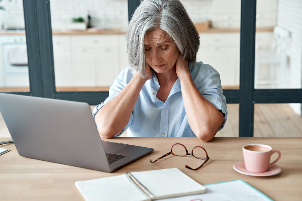 senior women with chronic pain, holding neck in front of laptop screen