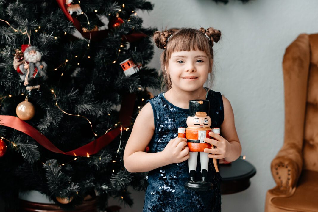 A,Little,Cute,Girl,In,A,Dark,Blue,Dress,Holds Girl, with down syndrome, holding a drummer in front of a Christmas tree