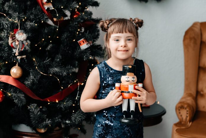 Girl, with down syndrome, holding a drummer in front of a Christmas tree