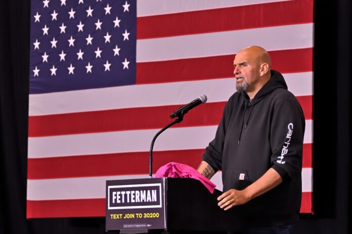 John Fetterman, standing at podium, in front of American flag