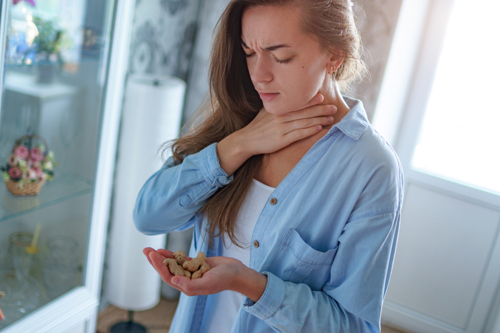 woman holding peanuts in one hand, with other hand on throat