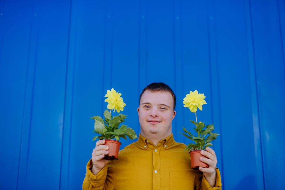 young man with Down syndrome holding up a yellow flower in each hand