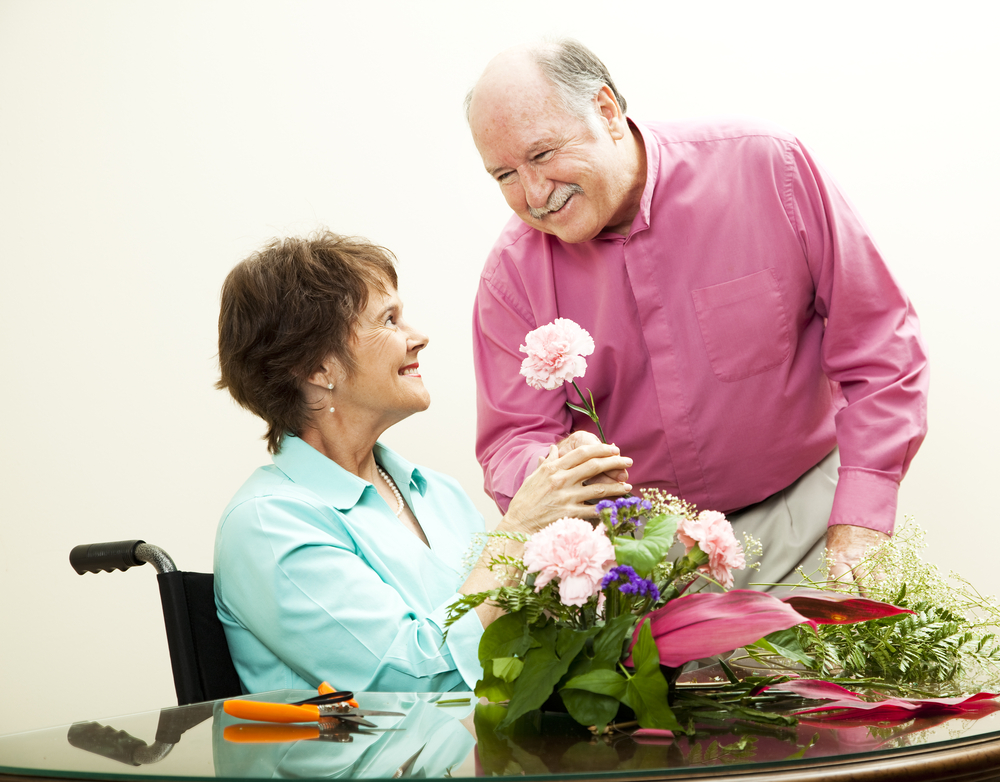 man handing a woman, who is a wheelchair user, a pink flower