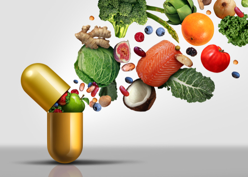 Vitamins, paired with a nutrient -rich diet, improve brain health. Image shows healthy foods popping out of a pill capsule. 