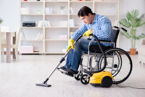 Man, a wheelchair user, uses a long-hosed vacuum.