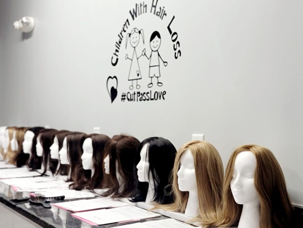 Row of real hair wigs made by Children With Hair Loss, an organization combating medically related hair loss