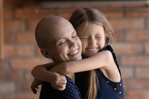 A young woman, with medically related hair loss, hugs a young girl