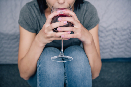 Mommy Wine Culture is on the rise. Photo: mom sipping red wine while seated on floor with back up to bedside. 