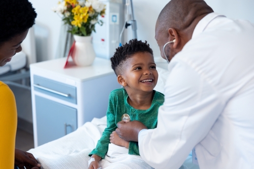 A child, sitting in a hospital bed, smiles at his physician.