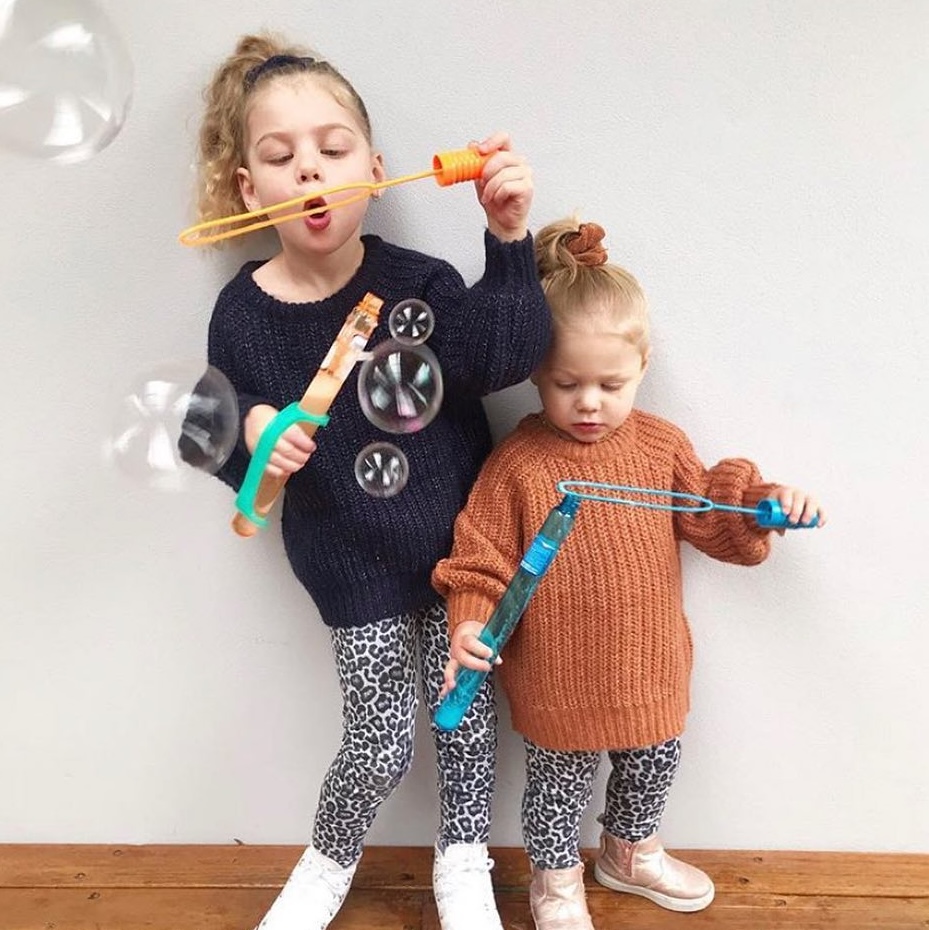 Two young girls using EaZyHold cuffs to hold onto bubble containing while blowing bubbles