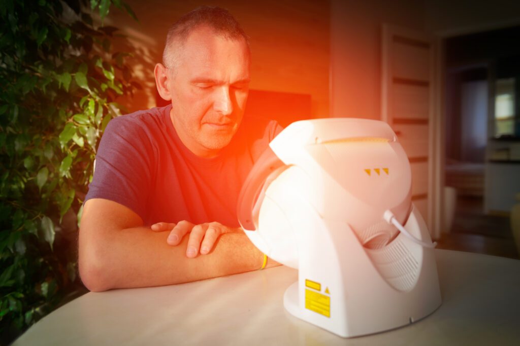 Man treating pain in the sinuses and head with infrared light therapy. The man sits at the table near the healing lamp.