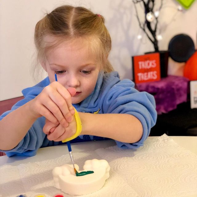 Young girl with hemiplegia using a yellow EaZyHold cuff to hold a paintbrush while painting
