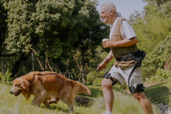 Senior man walking dog in wooded area using the Hypershell X Series Exoskeleton.