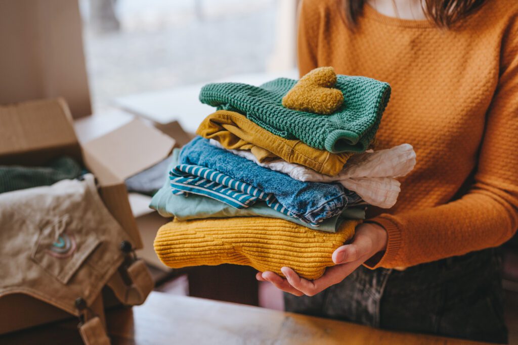 Close-up of female hands holding a fabric heart and clothes for charity.