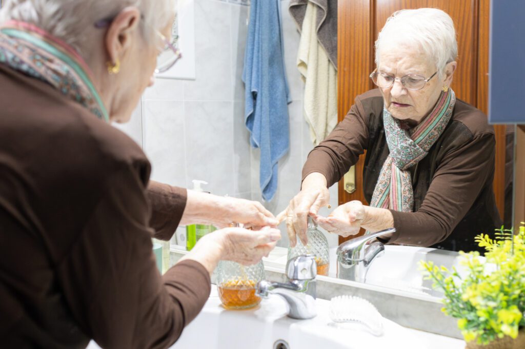 Senior woman washing her hands with liquid soap in the bathroom, gazing at her reflection in the mirror. Emphasizing hygiene and personal care in her daily routine