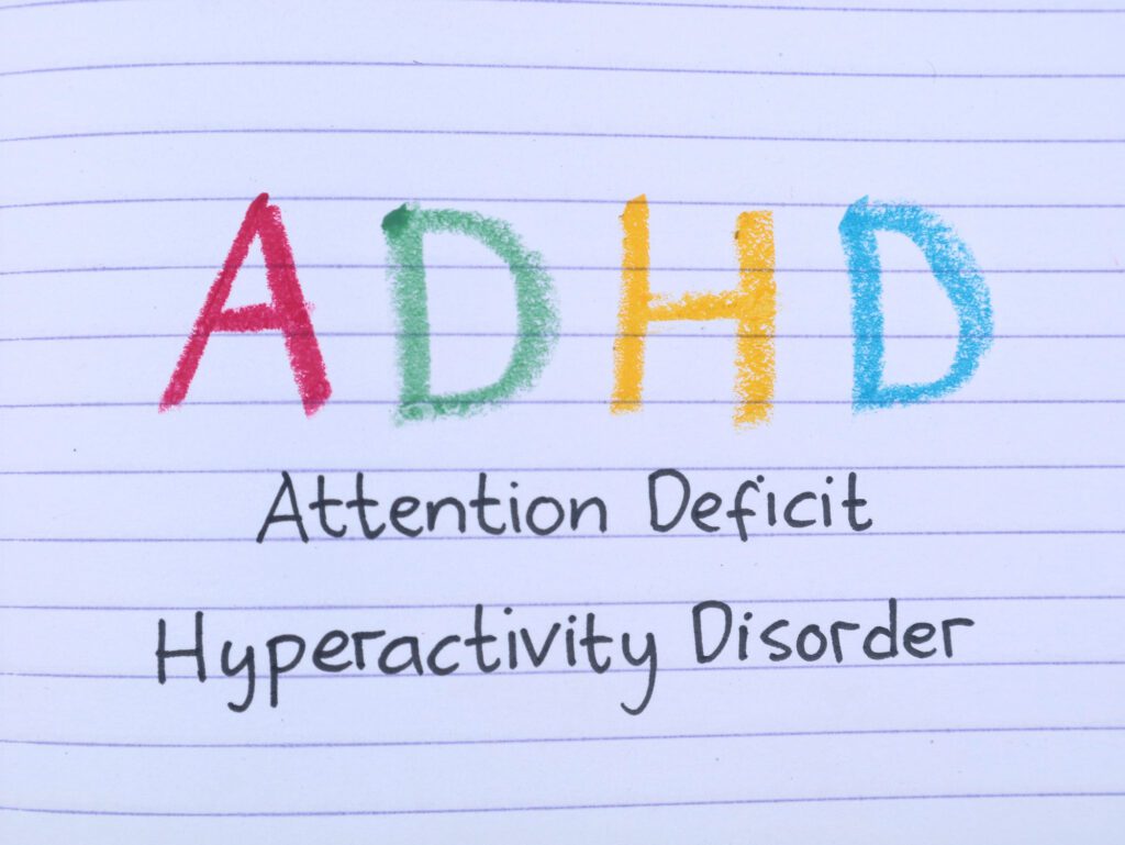 Handwritten text ADHD (Attention Deficit Hyperactivity Disorder) written with colorful letters on lined book paper. Concept for mental health, psychology, neurological condition, and education