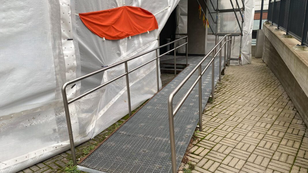 Temporary wheelchair access ramp with metal handrails at building entrance under renovation